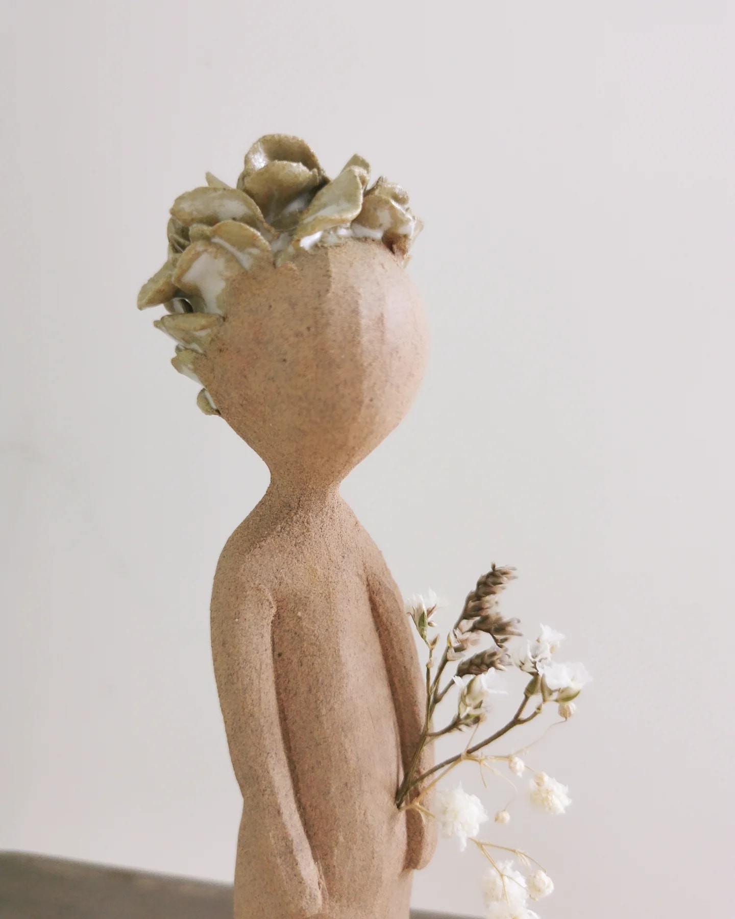 Figurine sculptée en grès brut avec couronne de fleurs en argile émaillée. Pièce unique Piriac