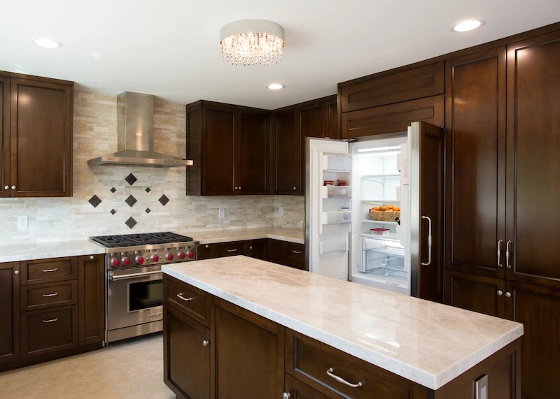 Kitchen with dark cabinets, stone backsplash, and open stainless steel fridge in Orange Interior Remodel.