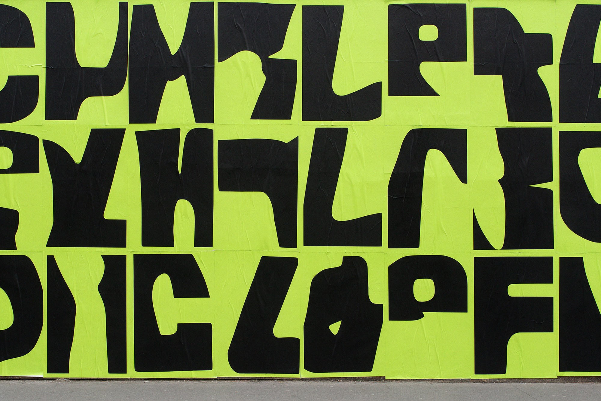 Wall of lime green posters printed with huge black letter-like shapes