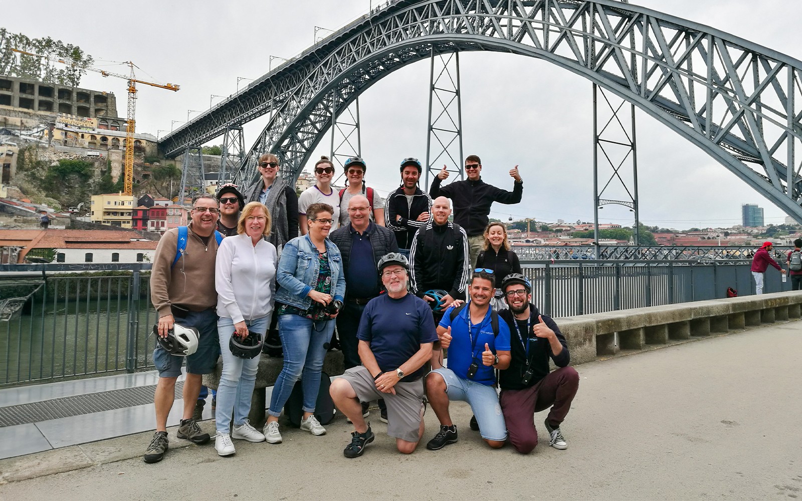 Grupo de ciclistas posando junto à Ponte Dom Luís I durante um passeio de bicicleta no Porto, Portugal.