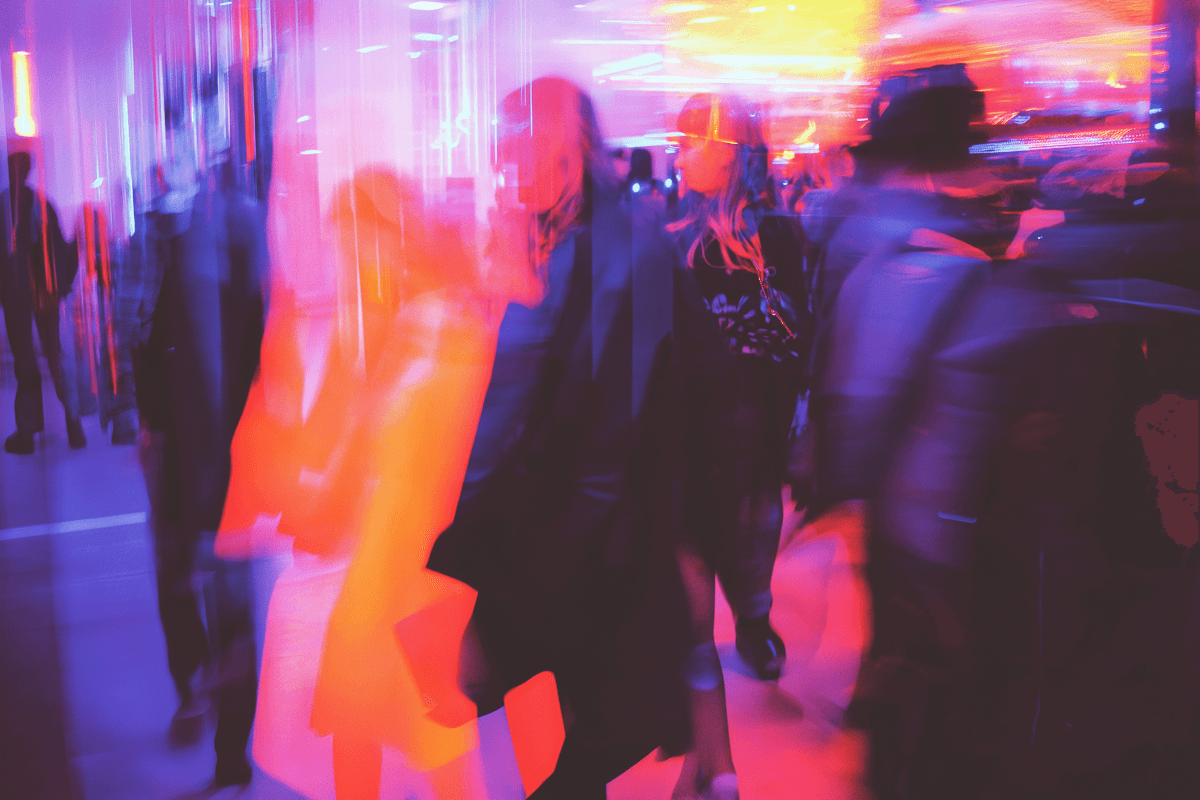Crowd of blurred people in motion, illuminated by vibrant, abstract city lights.