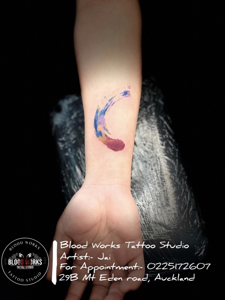 Vibrant tattoo of an abstract, multicoloured brushstroke resembling artistic paint swipes on the wrist. Tattoo artwork by Jai from Bloodworks Tattoo Studio, Auckland.