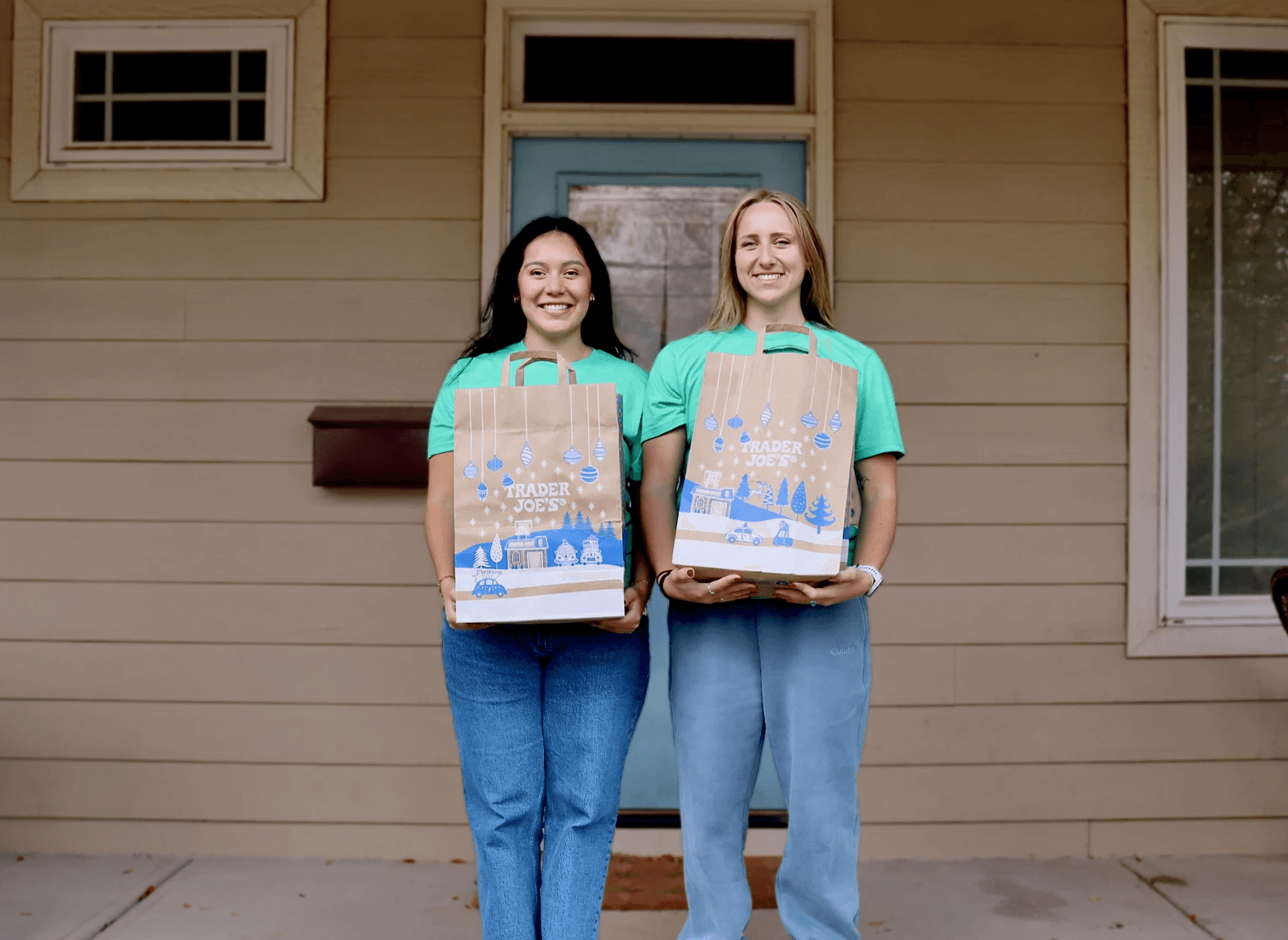 A young woman is handing grocery bags to an older man on his porch. Two other older adults are standing behind them.