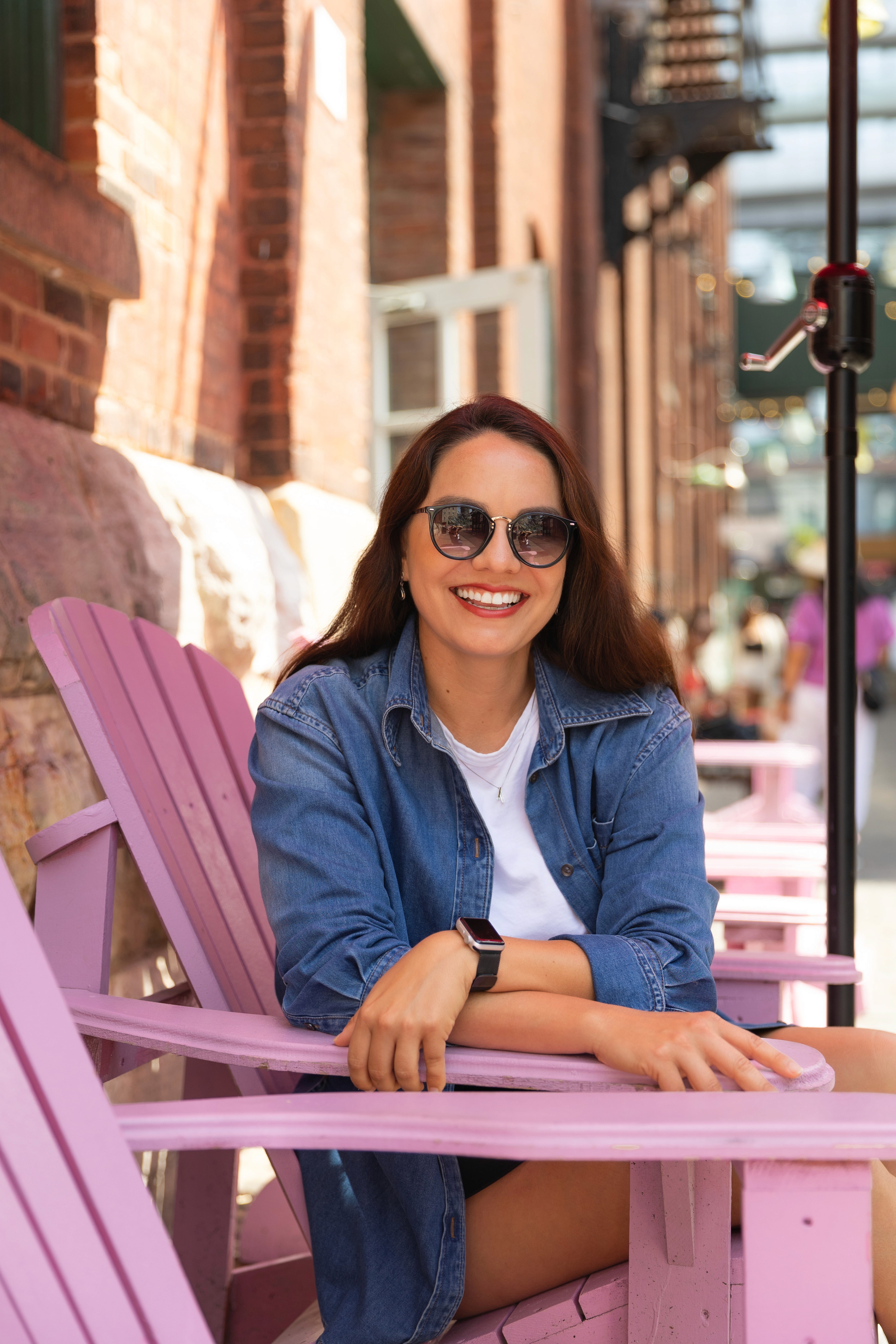 Mulher sorrindo sentada em uma cadeira rosa no Distillery District em Toronto, curtindo o dia ensolarado.