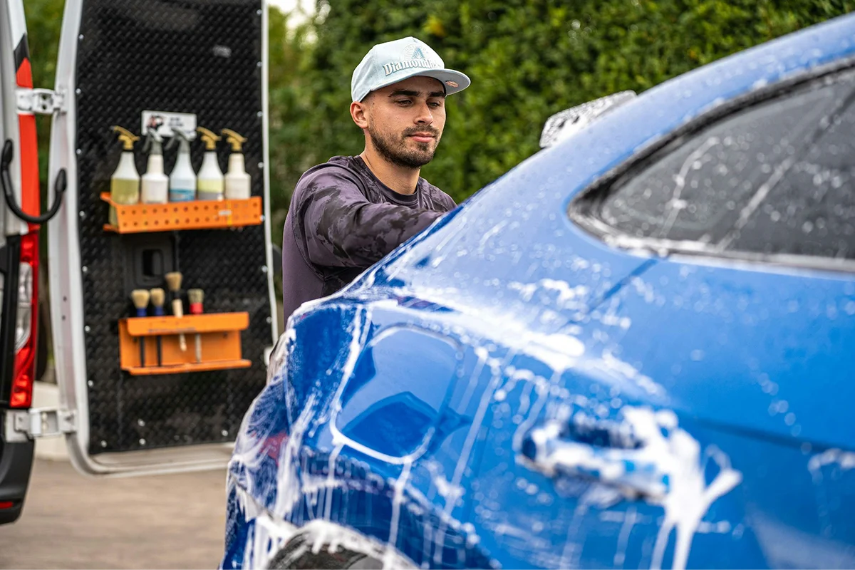 Technician washing a blue vehicle covered with soap and water
