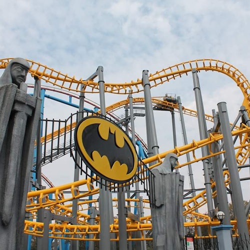 一條有黃色軌道和灰色支柱的過山車，擁有蝙蝠俠標誌和兩座類似石頭的雕像。