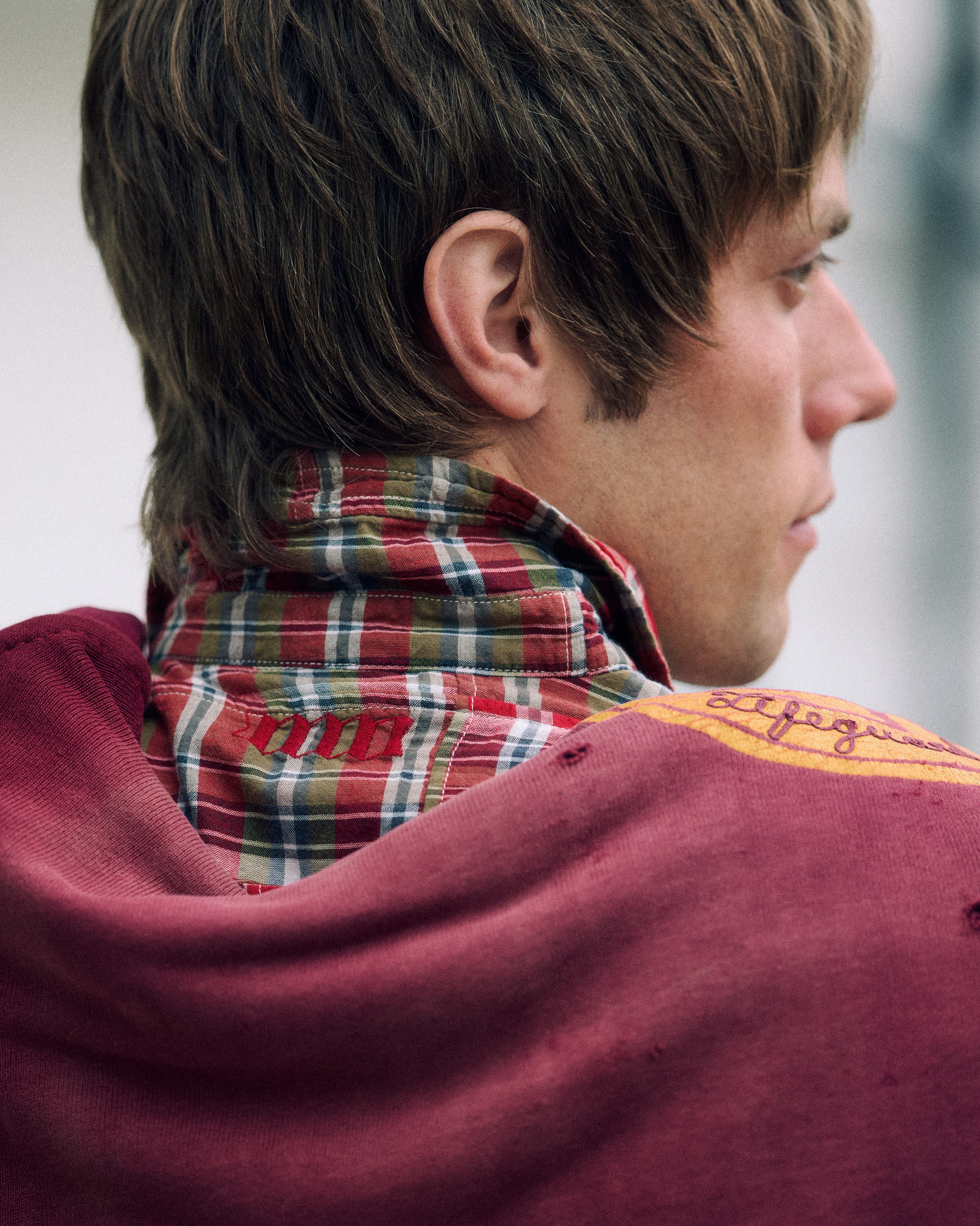 Détail de dos dans le lookbook Baracuta, avec chemise à colrelevé en tartan et pull bordeaux sur les épaules