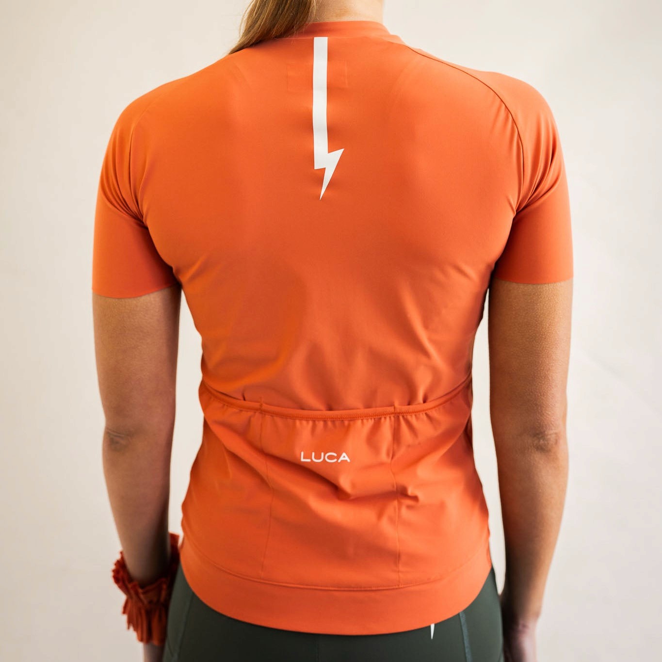 Cyclist wearing LUCA Soleil jersey in aperol, back view
