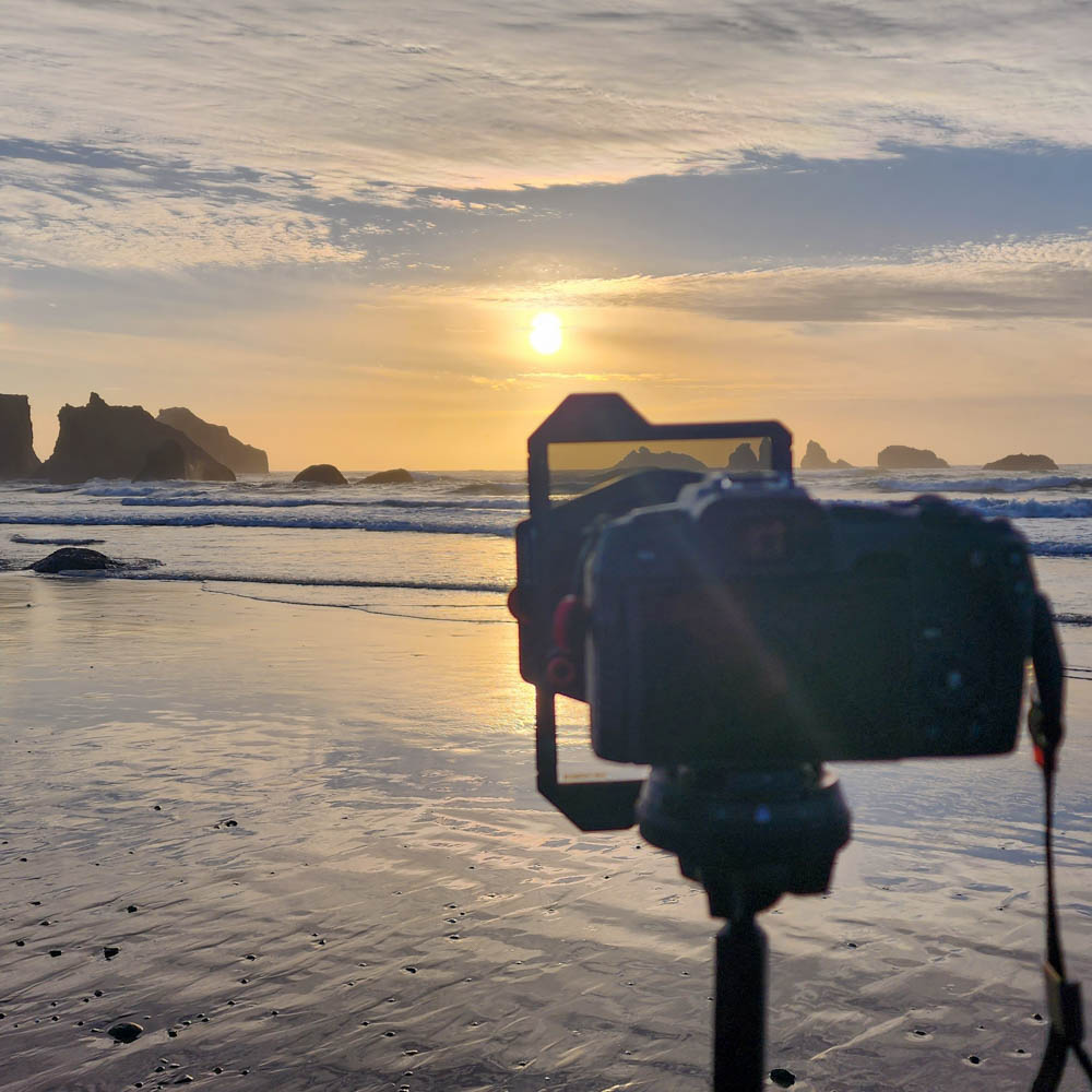  Camera on tripod aimed at the ocean during golden hour on a beach with rock formations.