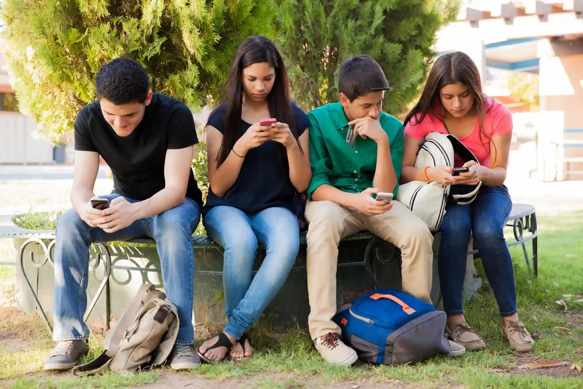 Four teenagers sitting outside, distracted by their smartphones, symbolizing a common struggle with digital distractions.