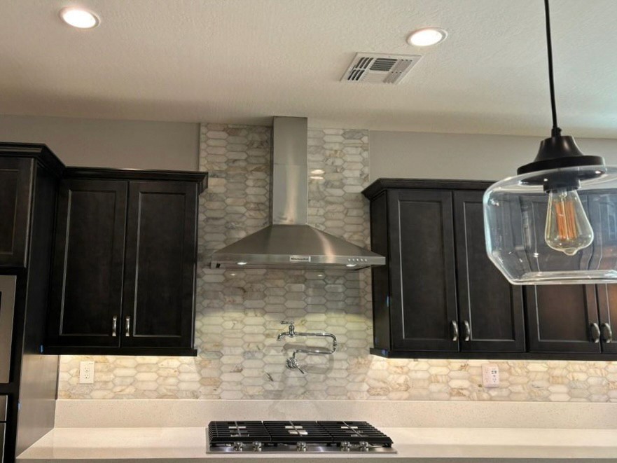 Contemporary kitchen with dark cabinets, a stainless steel range hood, and a herringbone tile backsplash.