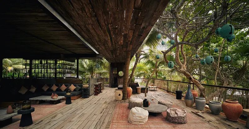 Sky Terrace restaurant at Be Tulum: covered terrace surrounded by seating options like poufs, sofas, and center tables for dining and drinking, amidst trees and selvatic zone.