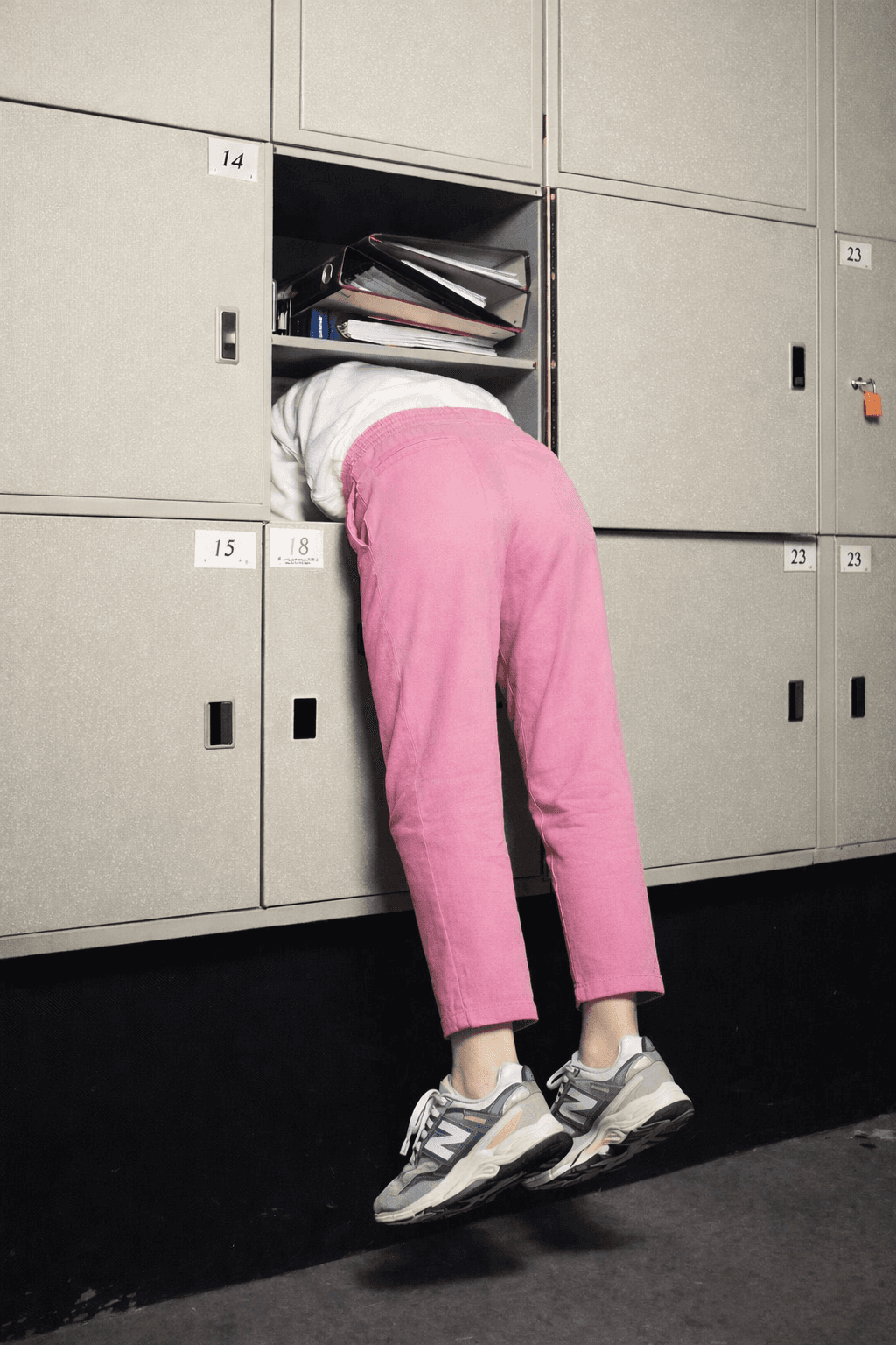 A person in pink pants leans into a locker, with only their legs visible from the waist down.