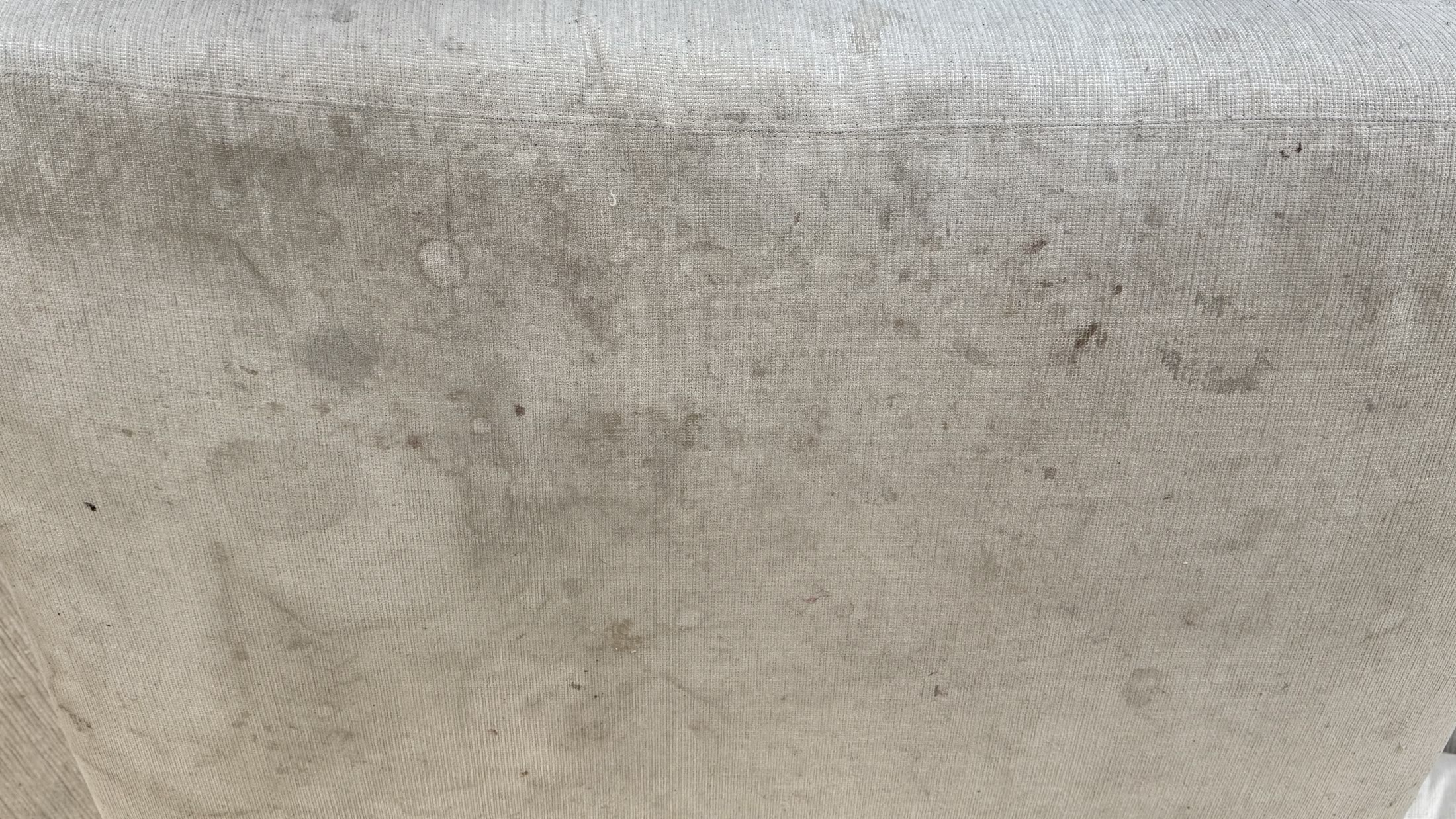 Close-up of a light upholstered sofa cushion with visible spots before cleaning.
