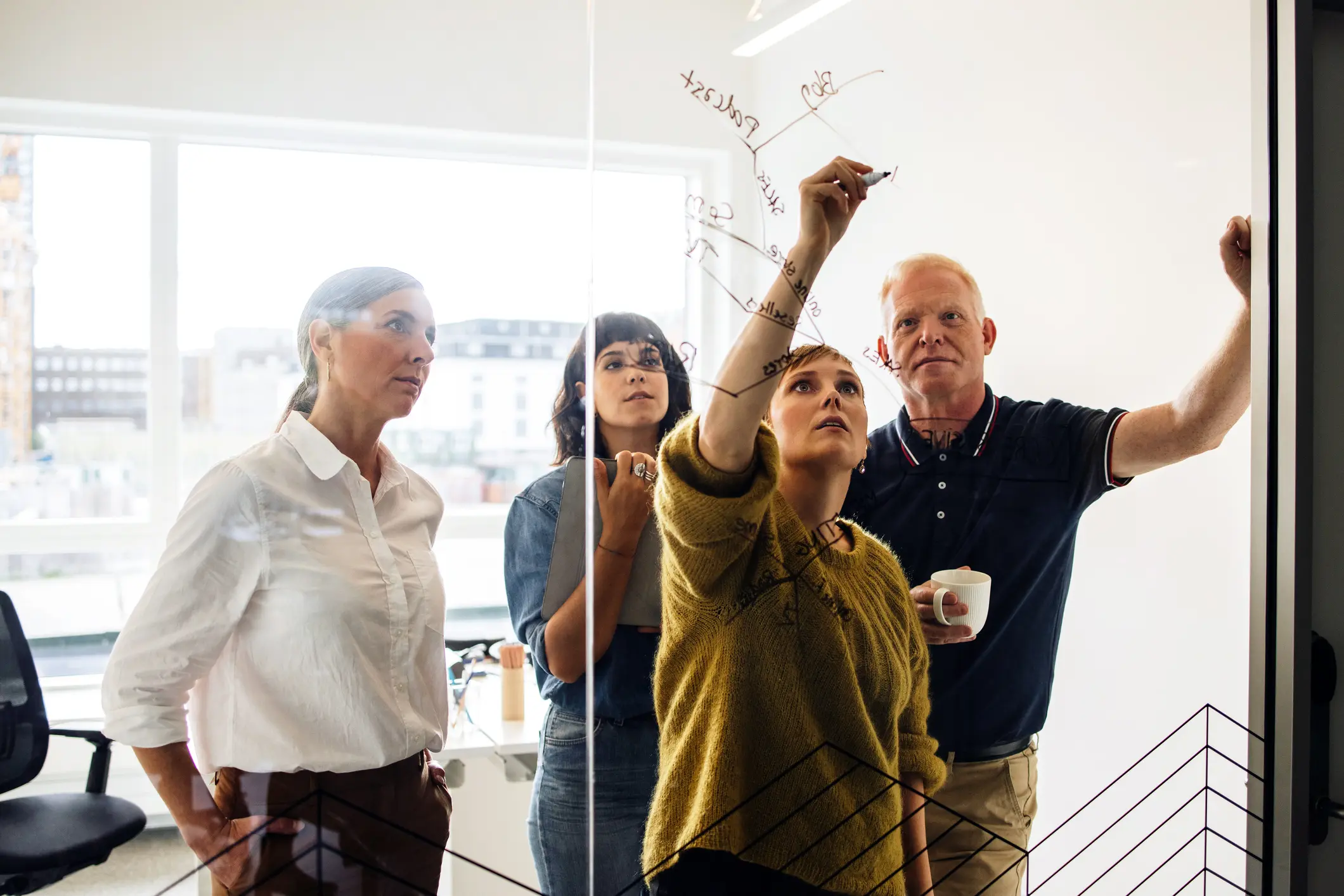 Four diverse colleagues collaborating around a glass whiteboard during a marketing strategy session