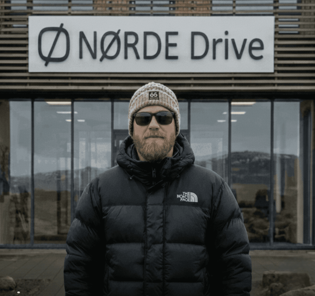 Man in a black puffer jacket standing outside a building with glass windows.