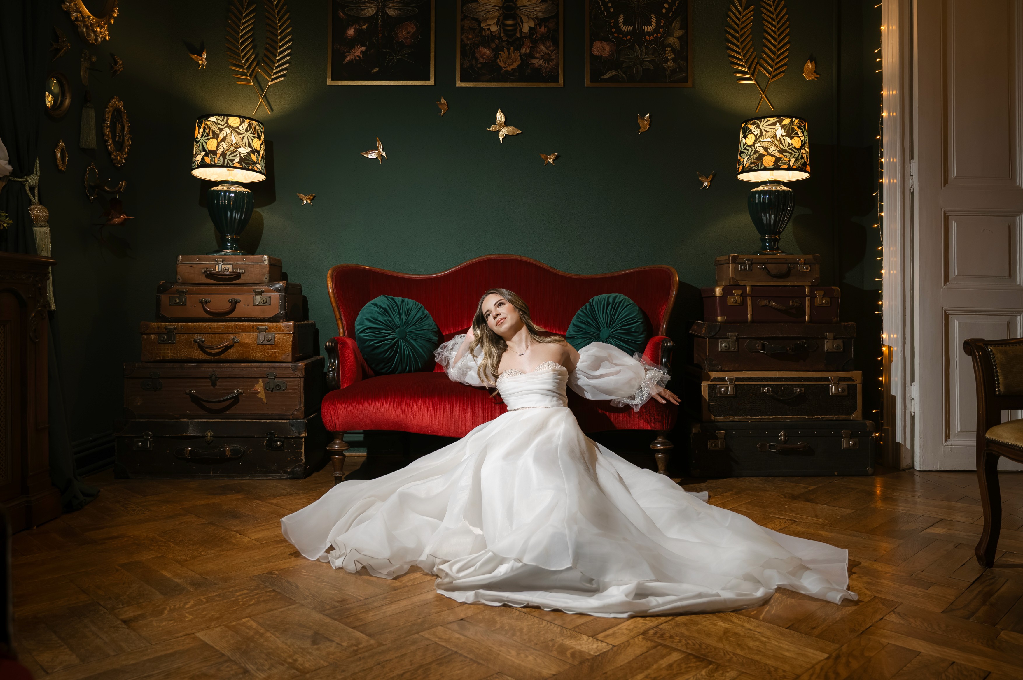 Mireasă în rochie albă amplă pe canapea roșie din catifea, decor vintage cu valize și lumânări, fotografie documentară de nuntă realizată de Radu Iordan fotograf de nuntă București