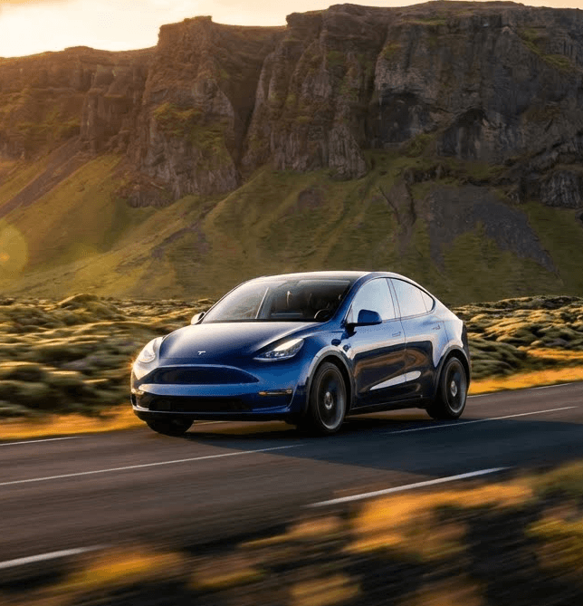 A blue sports car driving on a scenic road, with hills and a sunset in the background.