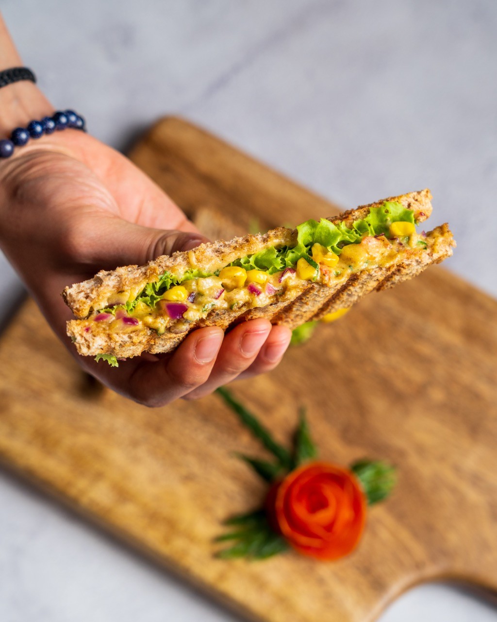Person with a mustache wearing a black t-shirt carrying a tall stack of pizza boxes inside a dimly lit bar or restaurant.