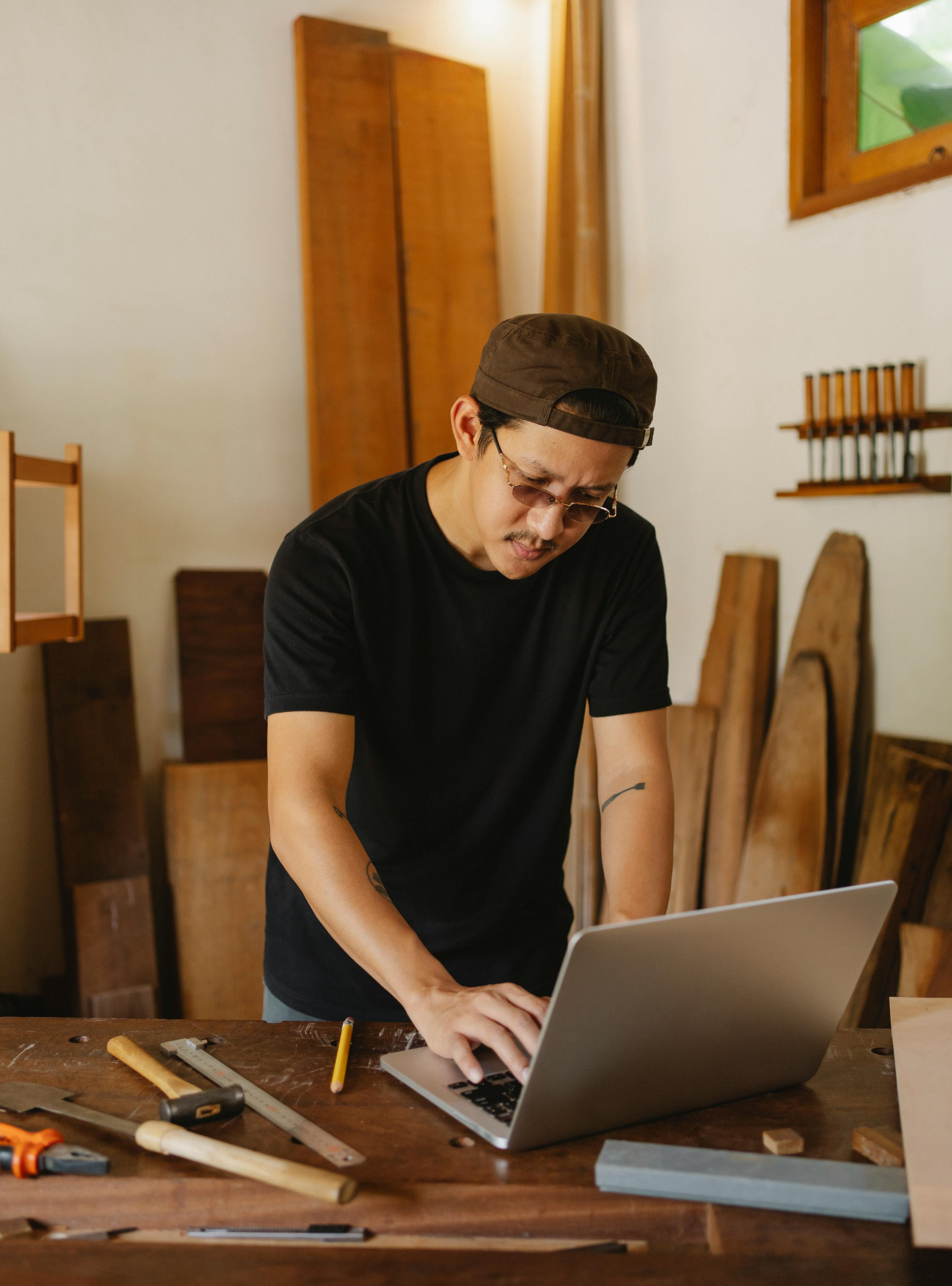 Uomo in laboratorio che lavora al computer circondato da attrezzi e legno, simbolo di artigianato digitale e trasformazione tecnologica delle professioni.