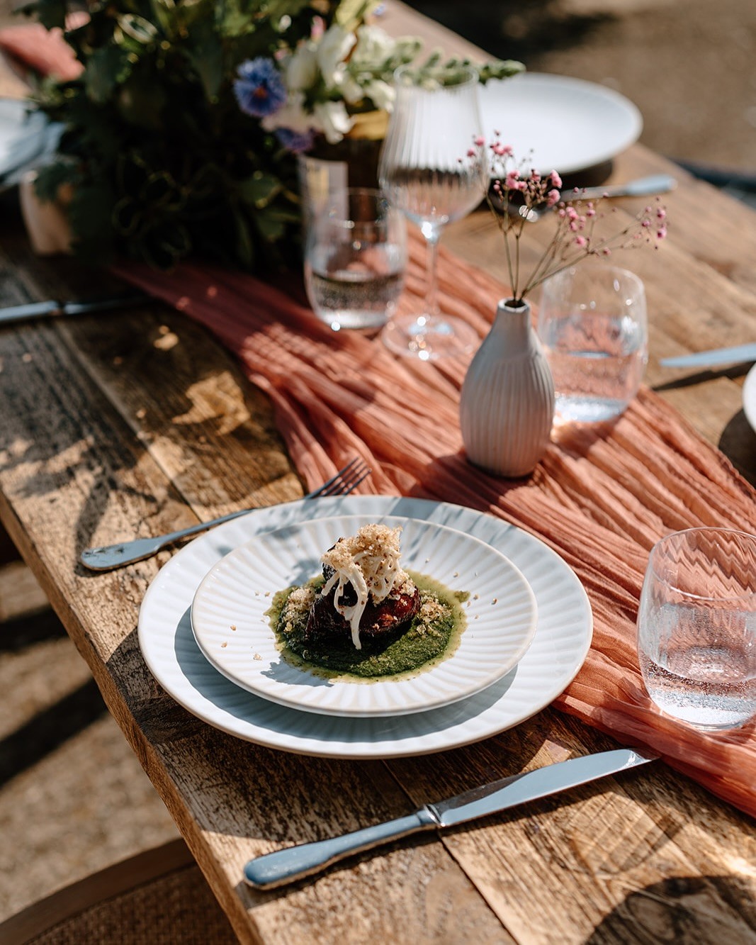 Close-up of a beautifully decorated dining table with a plate of food, flowers, and glasses. Rustic wooden table.