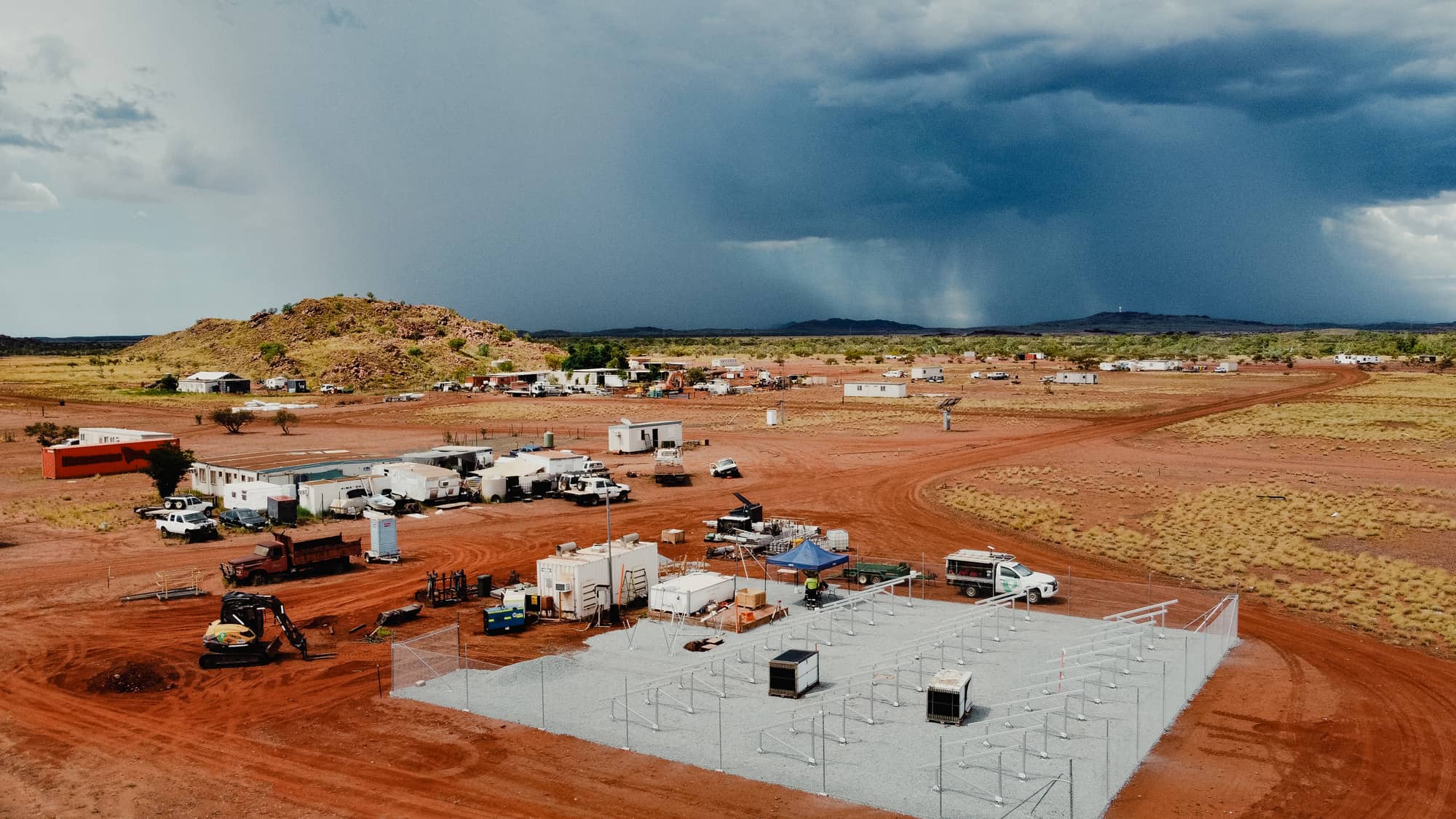 Construction of a renewable energy system in a remote, arid Australian landscape with a storm approaching.