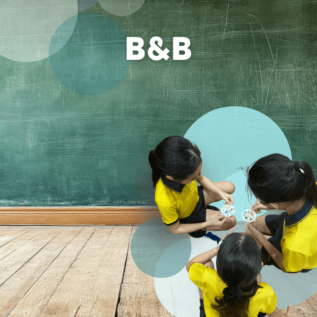 A young person with curly hair smiles at the camera while sitting in front of a laptop against a dark background.
