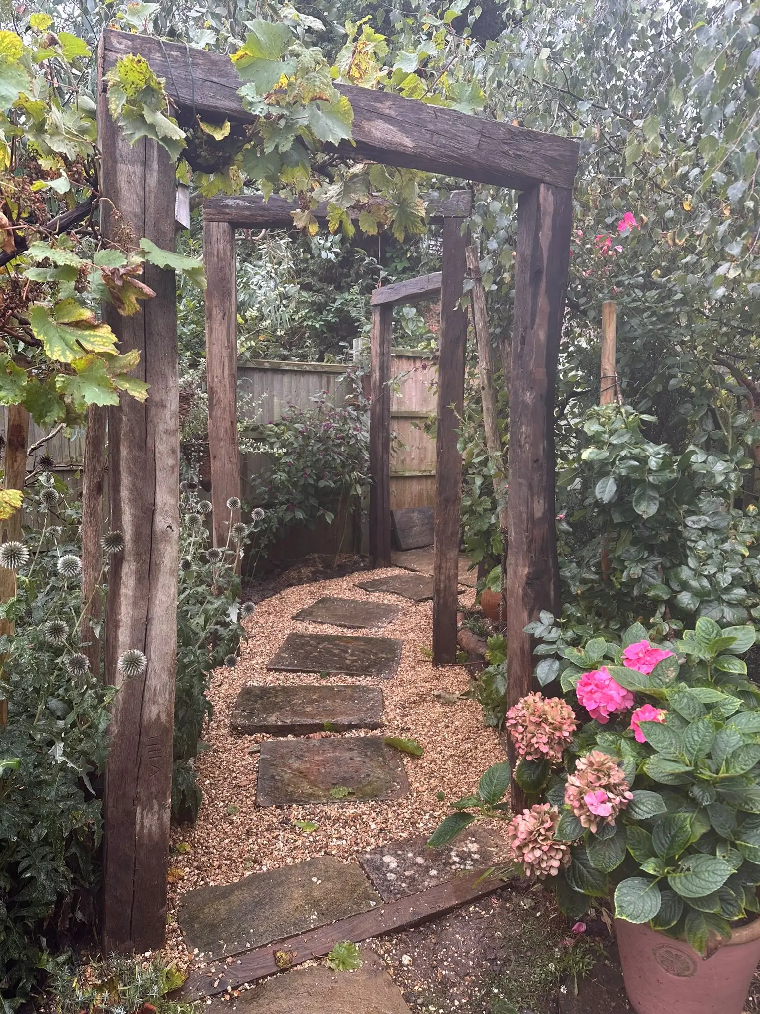 A serene garden path leads through an archway, surrounded by lush greenery and blooming flowers.