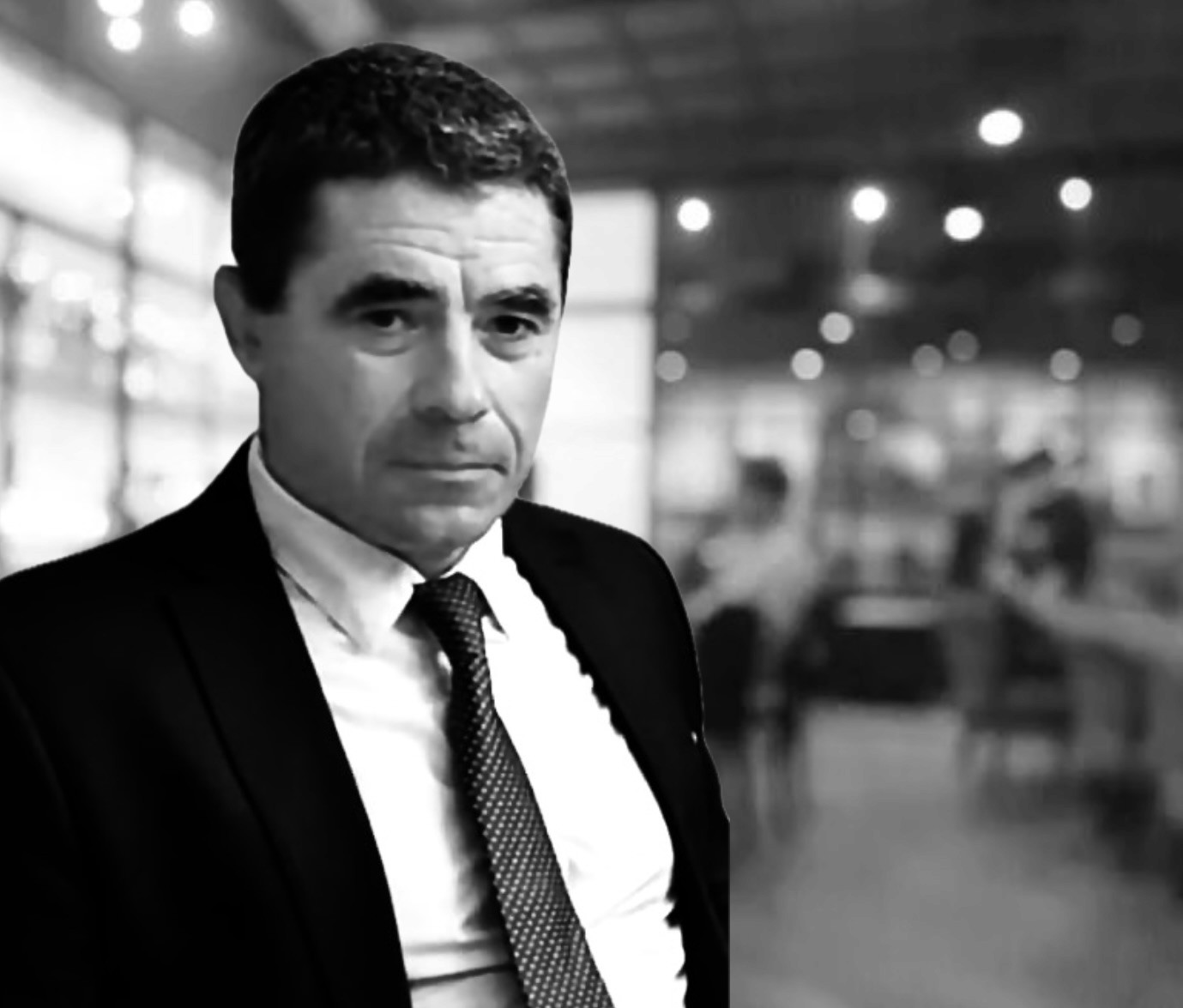 Black and white photo of a cauzazian man dressed in suit and tie with a blured office background