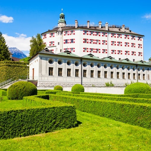 Jardins bem cuidados com sebes, topiárias e um grande edifício ao fundo sob um céu azul claro.