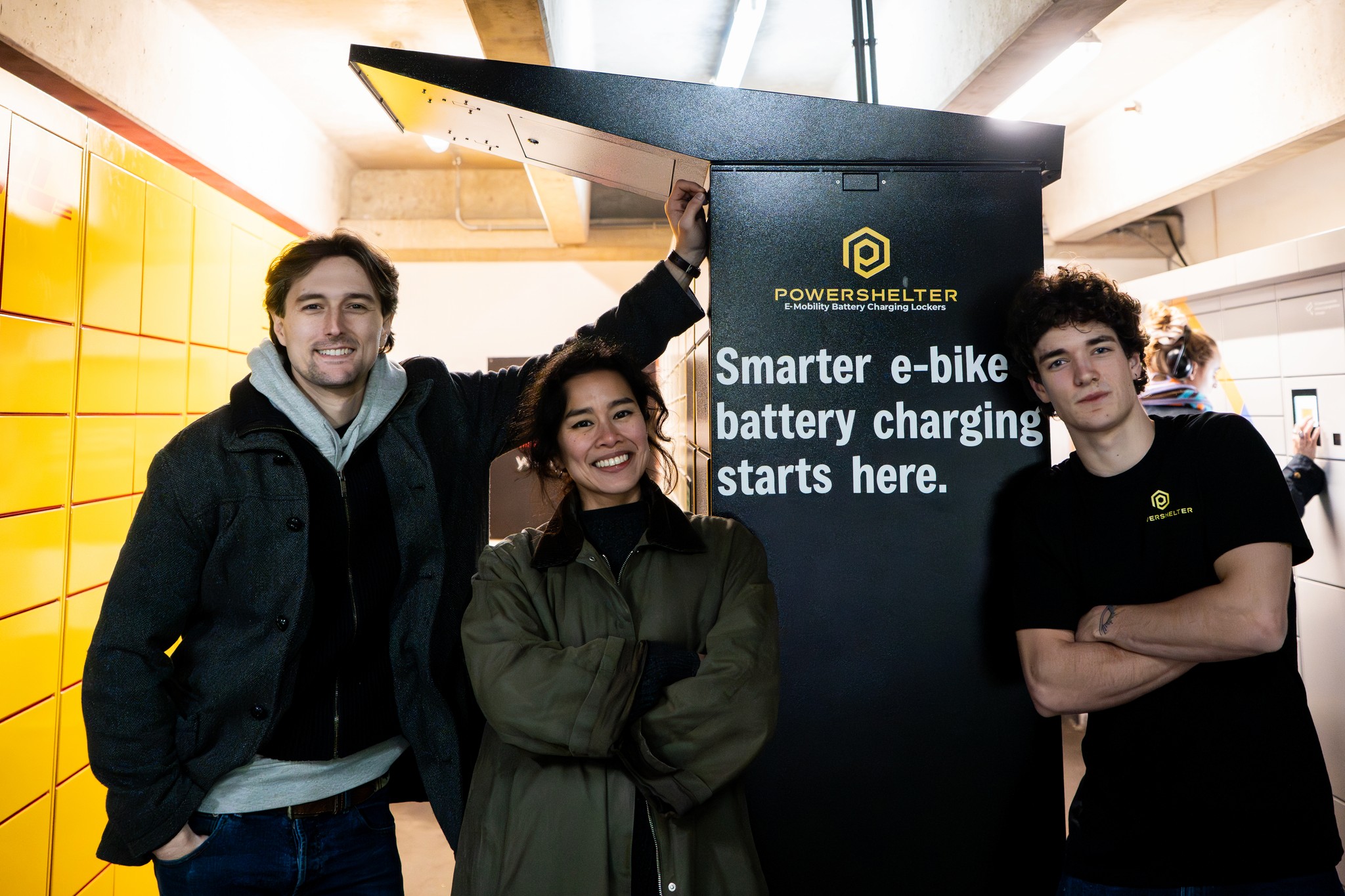 A person placing an e-bike battery into a charging locker, with charging cables connected and a digital display visible on the locker unit.