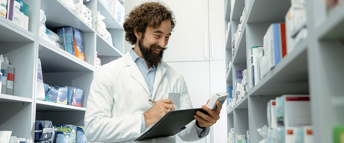A researcher in a lab coat reviews notes on a clipboard, surrounded by shelves of books or research materials.