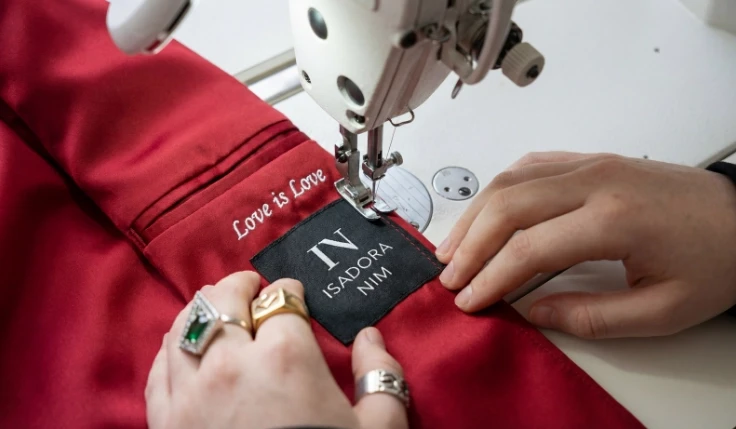 Tailor sewing an ISADORA NIM label onto a red garment