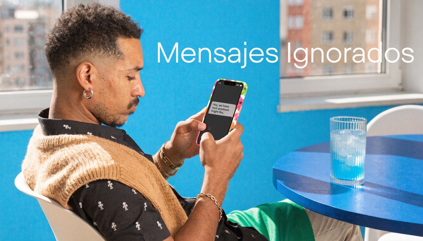 Un hombre joven revisa mensajes en su teléfono móvil mientras está sentado en una mesa azul.