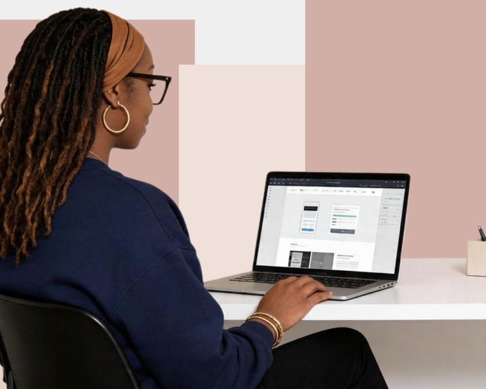 A person with long hair sitting at a desk, using a laptop with a minimalist workspace.