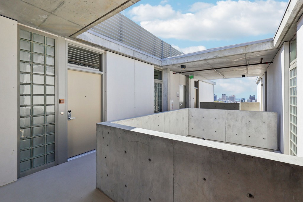 Modern concrete apartment corridor with glass block walls and metal doors, overlooking San Diego’s city skyline.