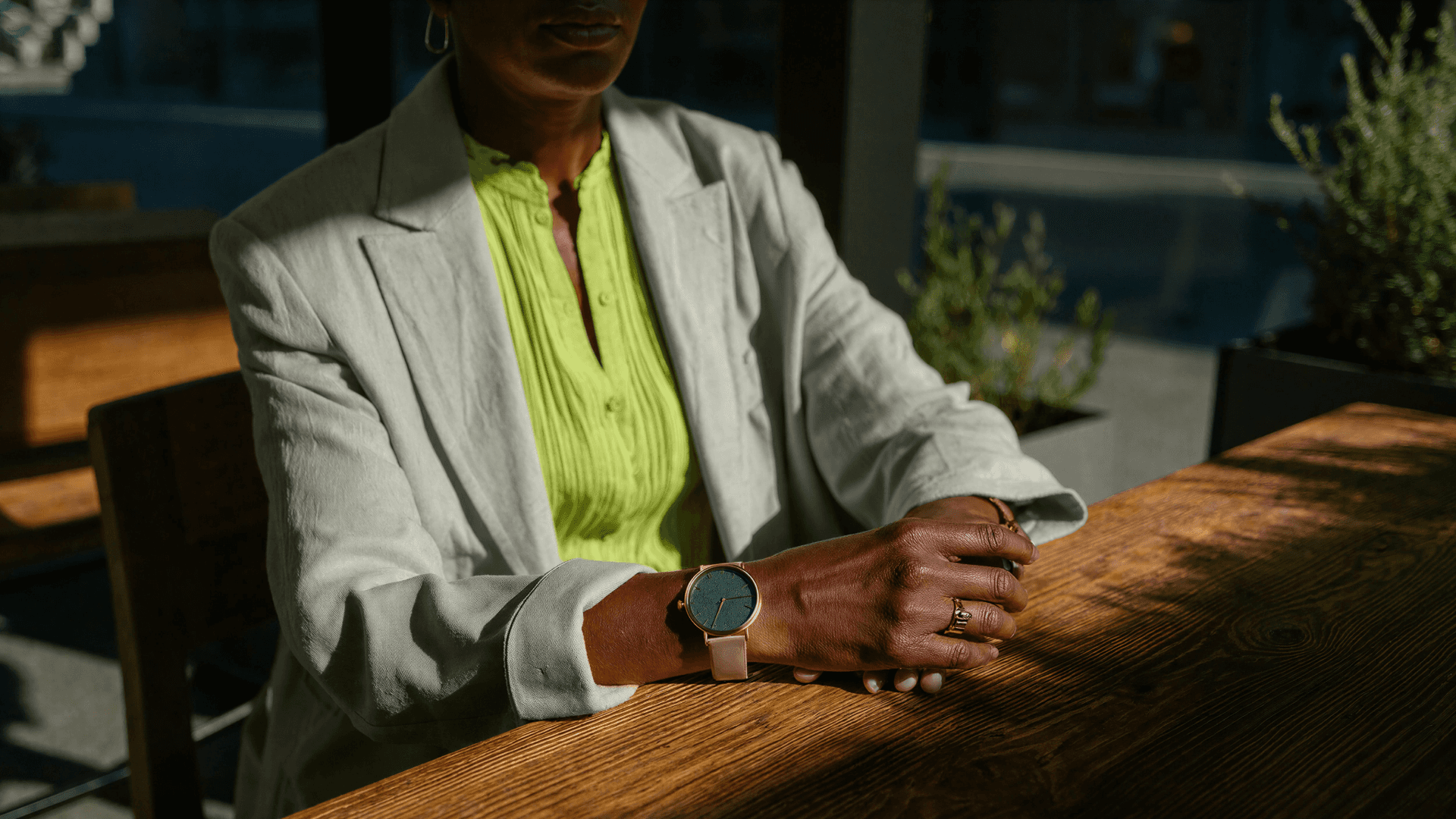 Gestora com relógio no pulso apoiada em mesa de madeira, representando controle de tempo e organização na gestão de clínicas com a Tivita