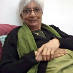 A young woman with long hair smiles while standing against a green backdrop, wearing a casual dark sweater.