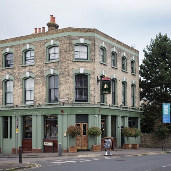 A smiling man with curly hair is sitting at a desk, looking at the camera, with a laptop and a lamp in the background.