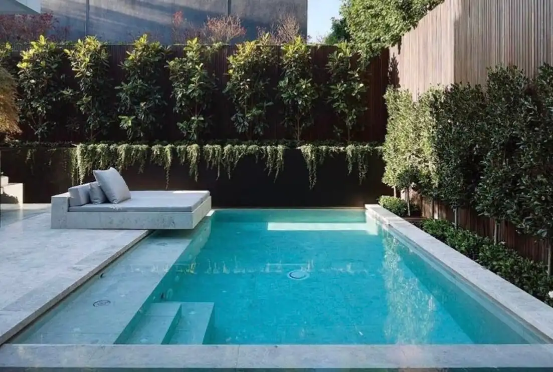 Espectacular pileta minimalista de lujo en patio interior, con plataforma de descanso flotante y bordes de mármol travertino premium.