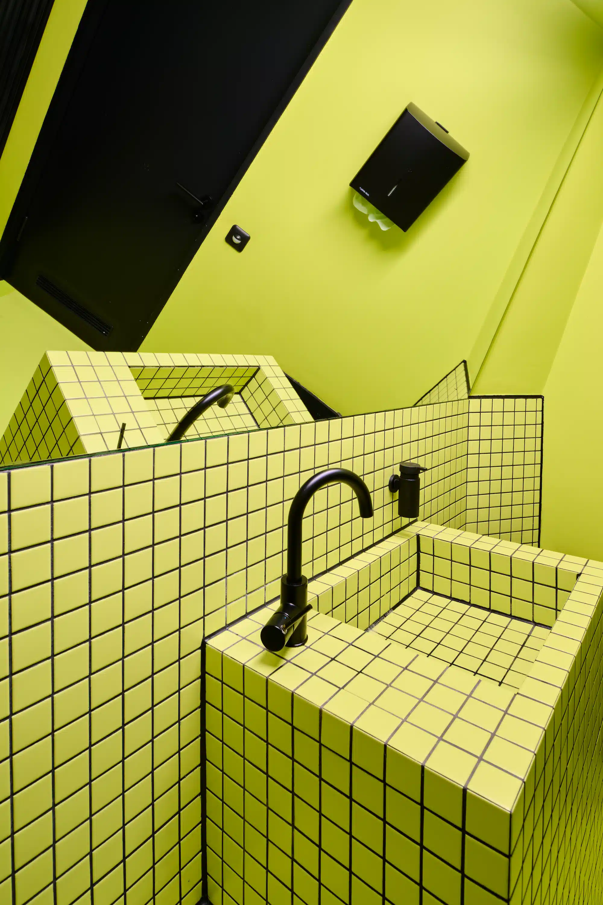 Dojo Office – restroom with completely neon yellow tiled walls, black fittings and vaulted ceiling