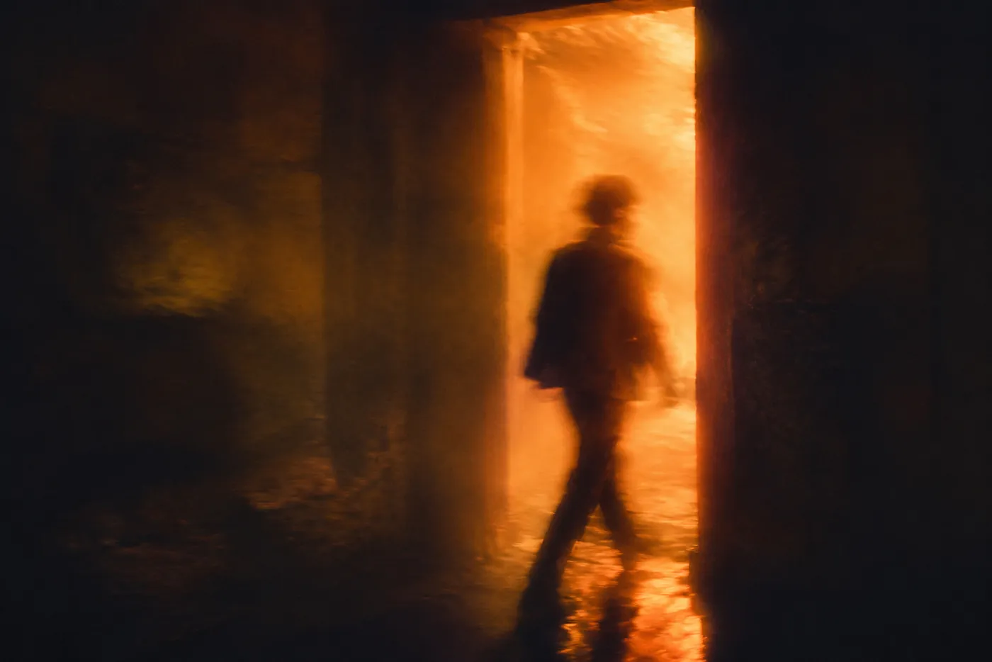 Silhouette of a person walking through a glowing doorway into warm light