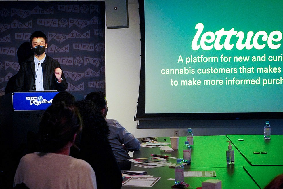 A man is presenting to the public while he has a projection with a text on the right side.