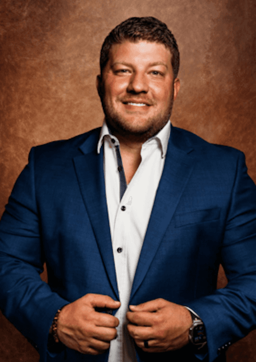 A man in a blue suit and white shirt stands confidently, representing professionalism in the real estate industry.