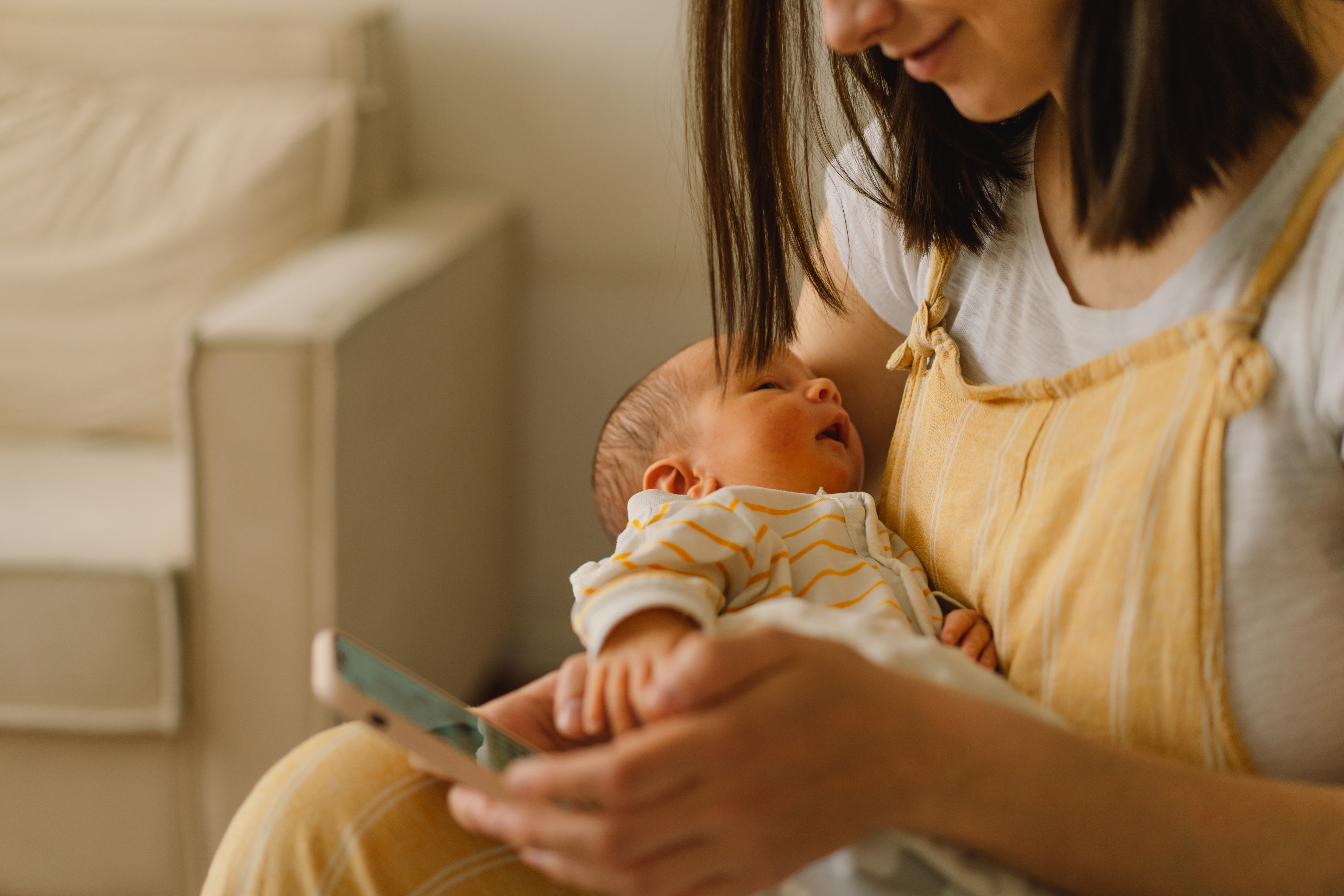 Mutter mit Baby im Arm und Smartphone in der Hand