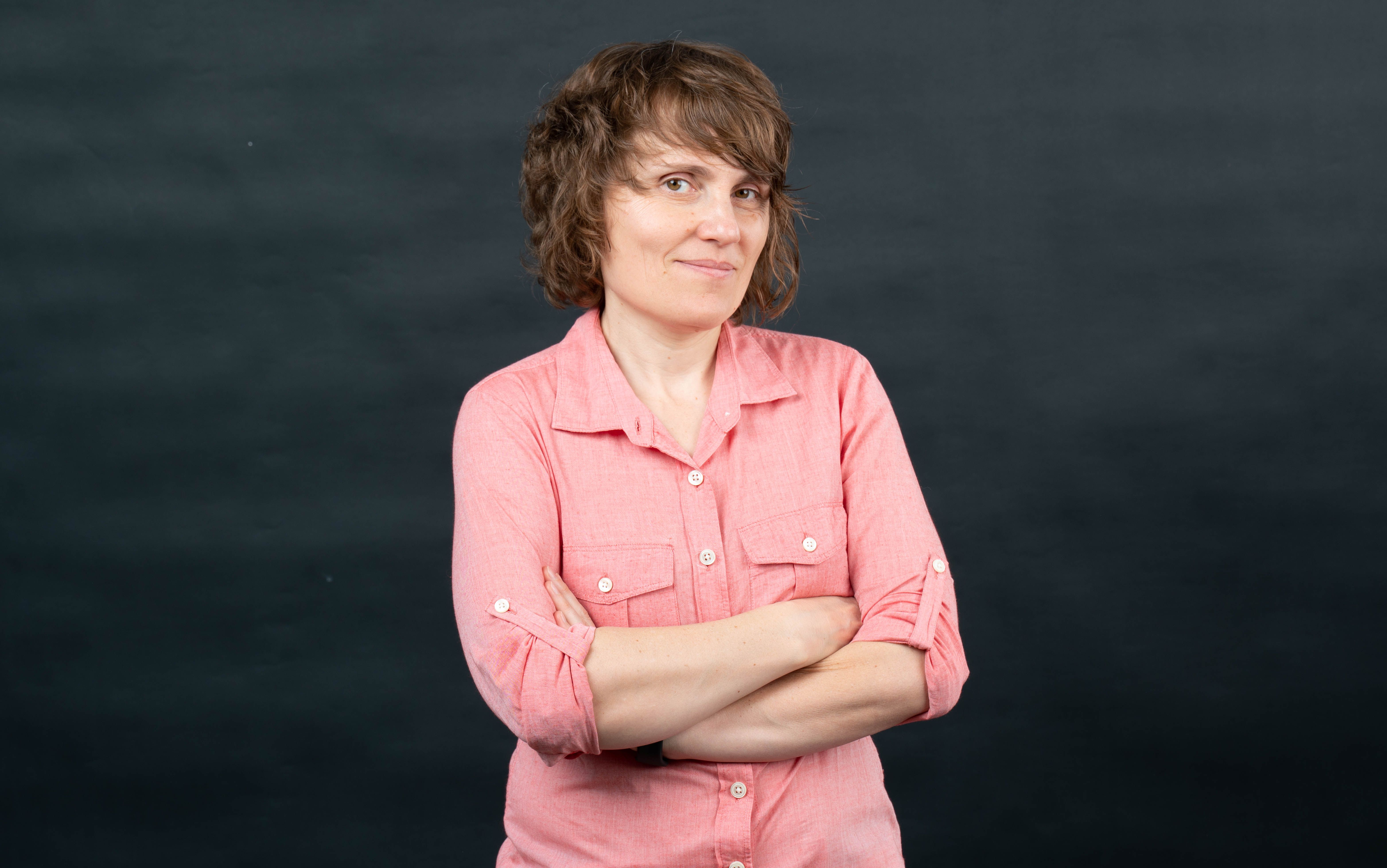 Adriana Georgescu, executive coach, smiling with arms crossed against a dark backdrop.