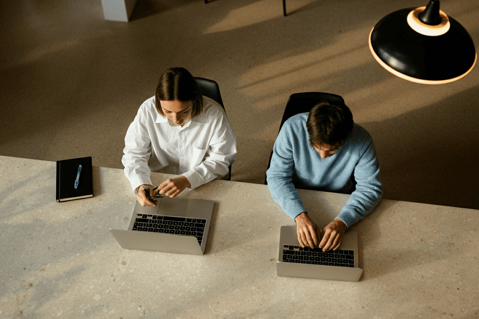 Young man in a green hoodie holding a yellow phone while seated at a table with a tablet.