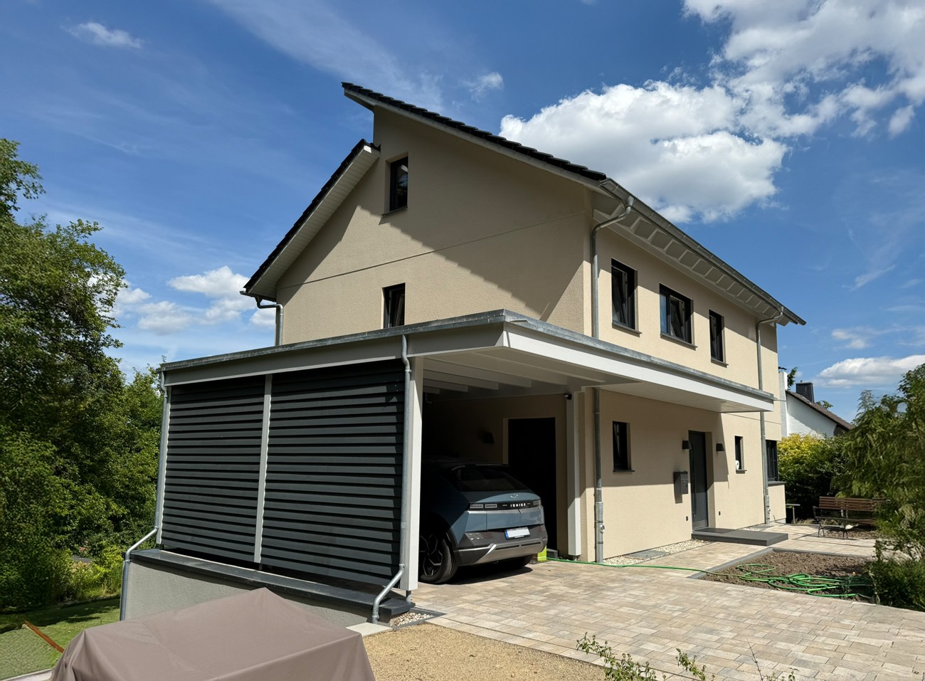 Modernes Einfamilienhaus mit Carport und barrierefreier Praxis im Untergeschoss – nachhaltige Planung für Arbeiten und Wohnen in Hanglage bei Bielefeld.