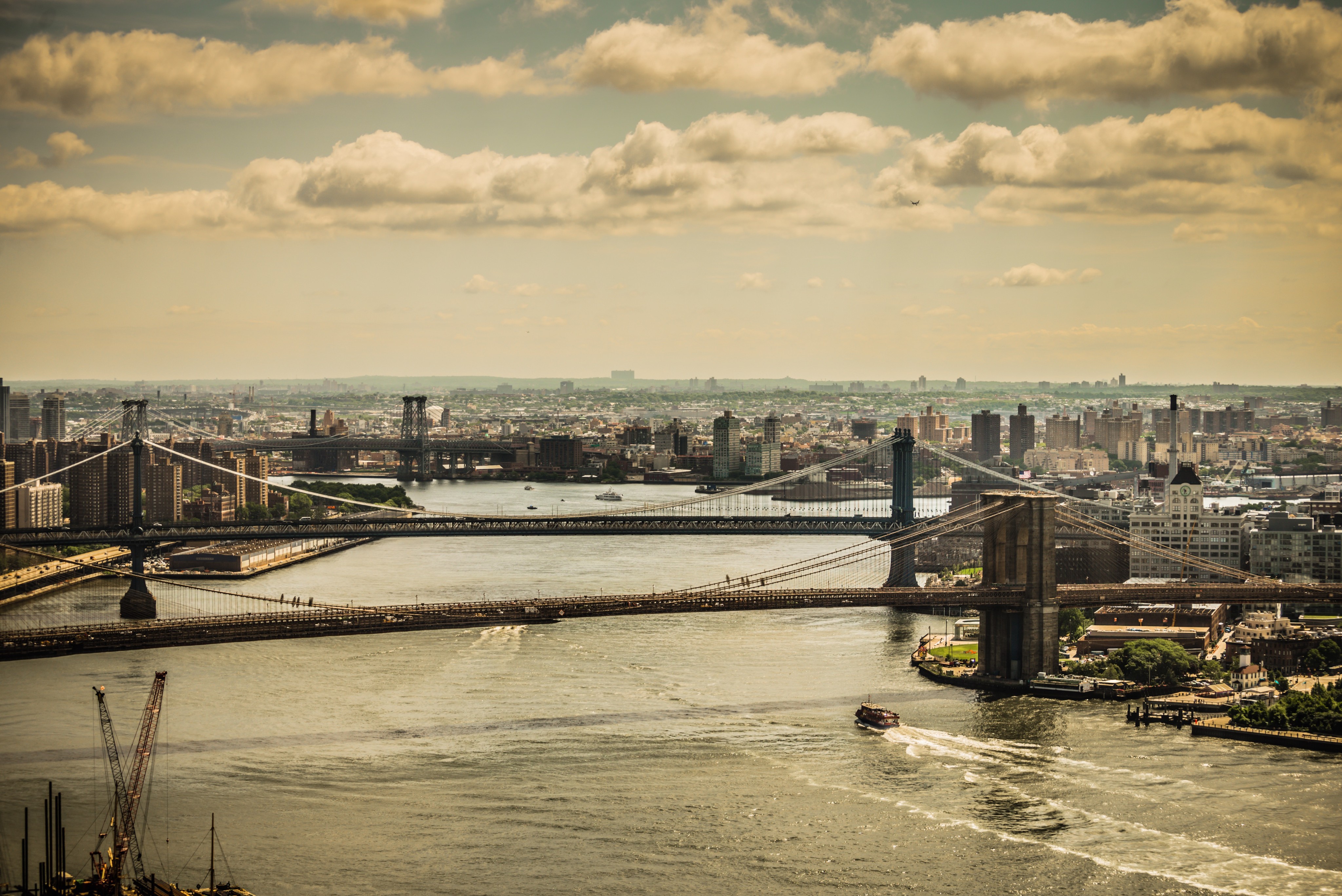 Aerial view of the East River in New York, featuring the Brooklyn Bridge, Manhattan Bridge, and Williamsburg Bridge.