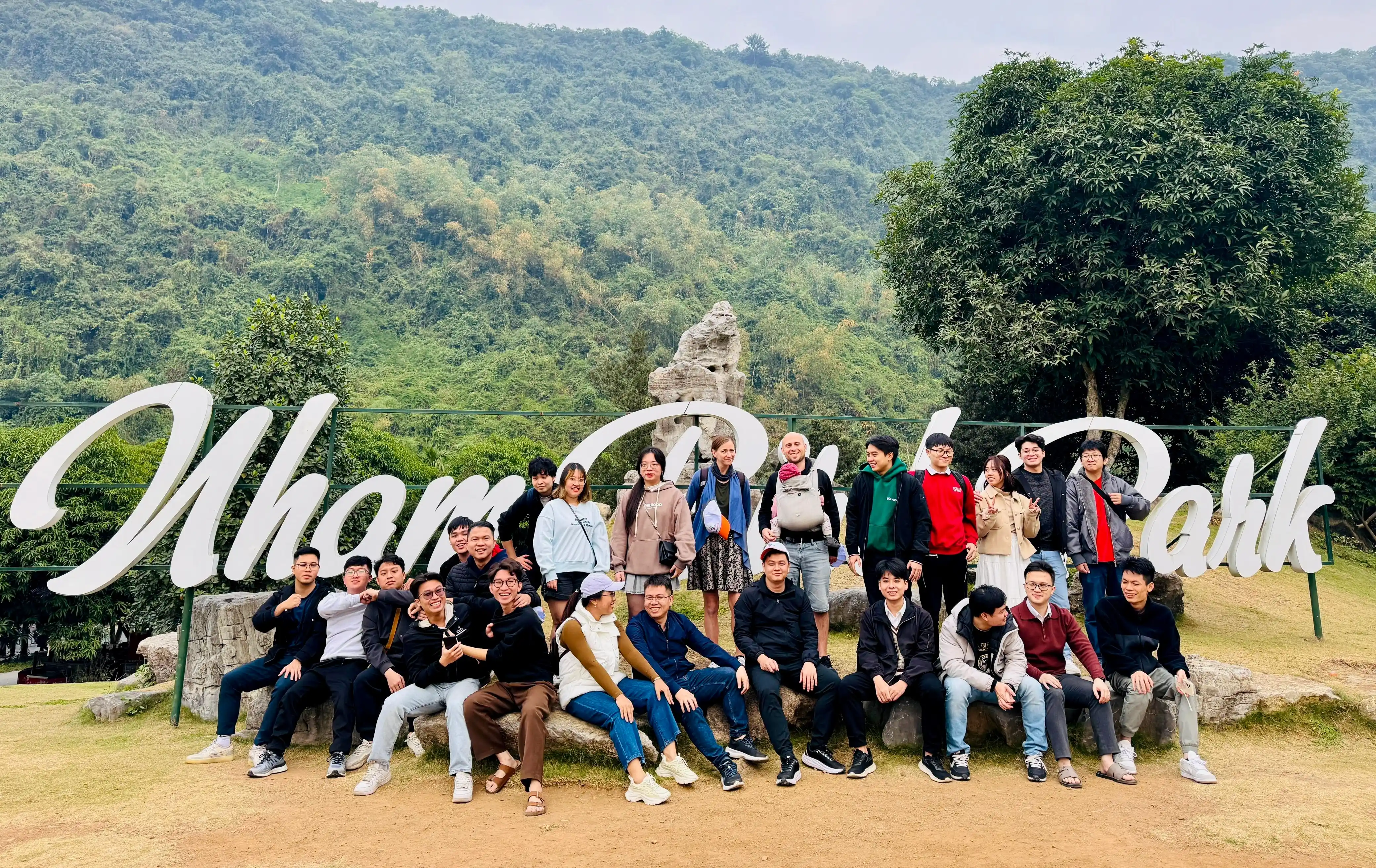 Group photo at Nham Park with large park sign and green hills in the background